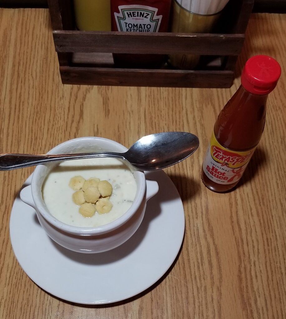 Bowl of clam chowder with oyster crackers next to Texas Pete hot sauce
