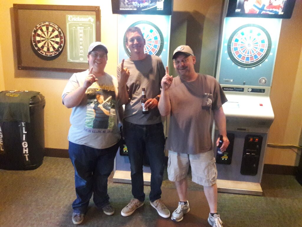 Three men holding up the number one after winning a three player dart tournament