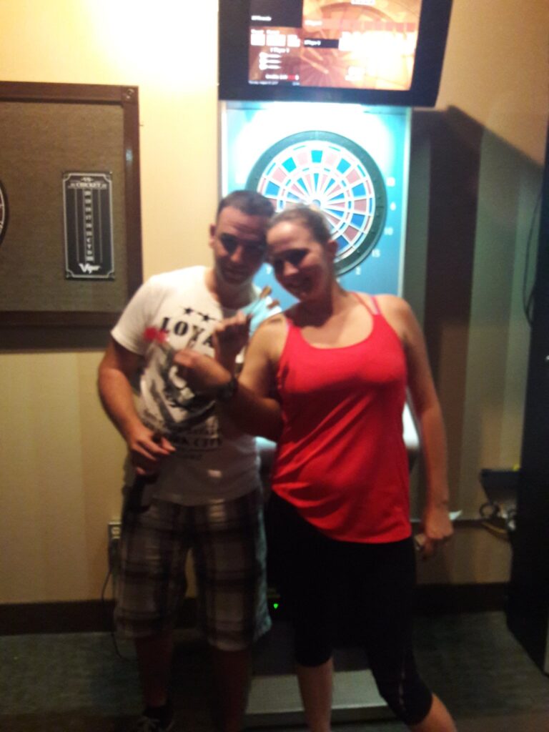A guy and a girl in front of a dart board after winning tournament
