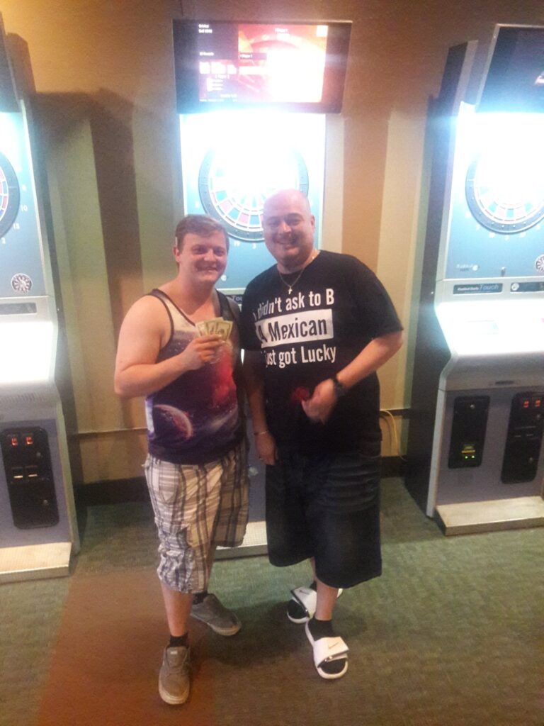 Two guys in shorts and tshirts celebrating winning a dart tournament