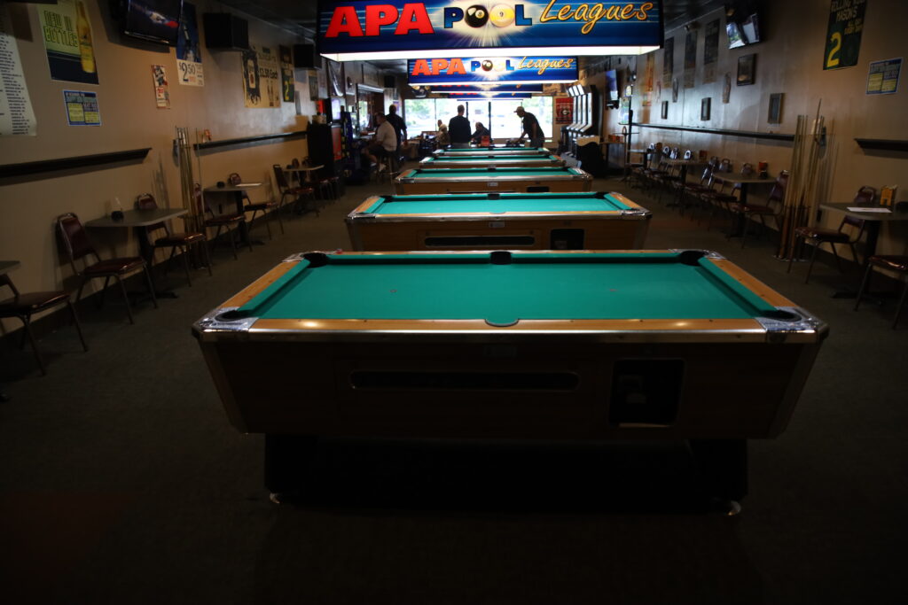 Row of green felt pool tables spanning the length of a bar's game room